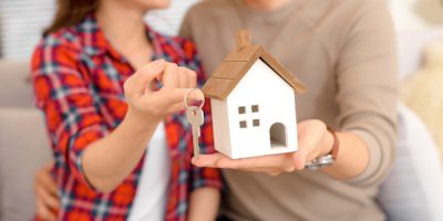 Happy couple holding keys to new home and house miniature - real estate concept